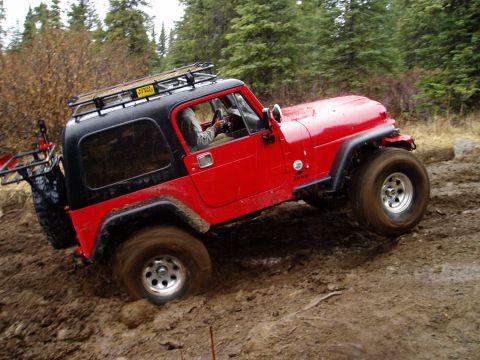 2000 Ford E350 - Red Jeep Wrangler navigating a muddy trail, tires deep in the muck.