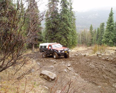 2000 Ford E350 - This vehicle navigates a challenging, muddy path surrounded by trees and rocks in a wooded area.