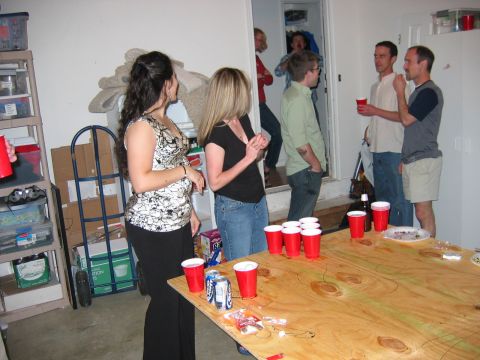 1985 Ford LTD Crown Victoria - A group of people are socializing in a garage setting with a table full of party supplies.