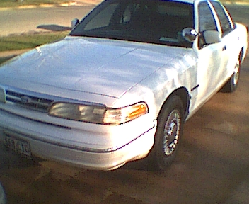1995 Ford Crown Victoria - A white 1995 Ford Crown Victoria is viewed from the front three-quarter angle, highlighting its distinctive grille and headlights.