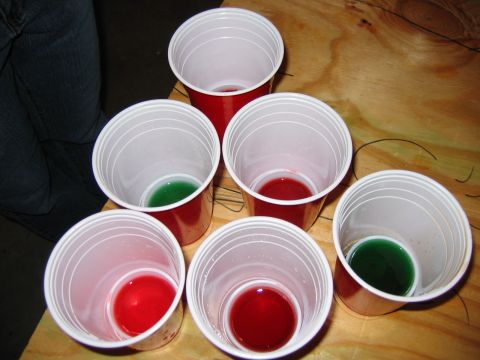 1985 Ford LTD Crown Victoria - Several red solo cups are set up on a wooden table, some containing red or green liquid.