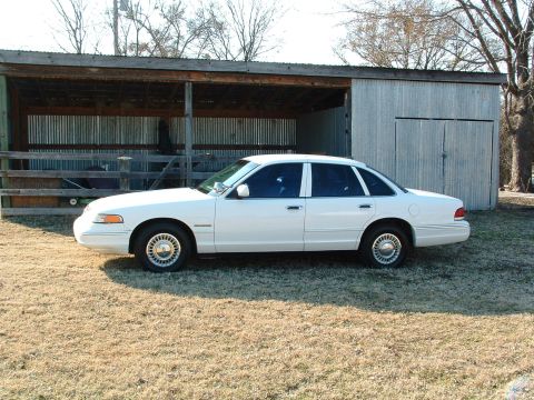 1995 Ford Crown Victoria - A white sedan is parked in front of a rustic shed with corrugated metal siding.