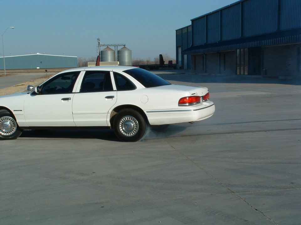 White 1995 Ford Crown Victoria doing a burnout, side view