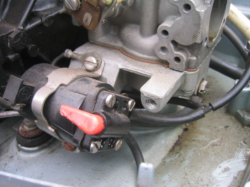 Close-up of carburetor with black electrical connector, red locking tab, and hoses