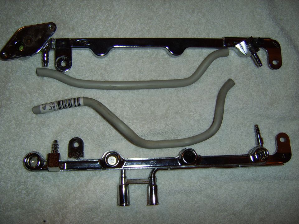 Two chrome automotive fuel rails and gray hoses laid out on a white towel