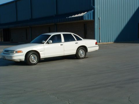 1995 Ford Crown Victoria - A white 1995 Ford Crown Victoria sedan is parked in front of a blue building.