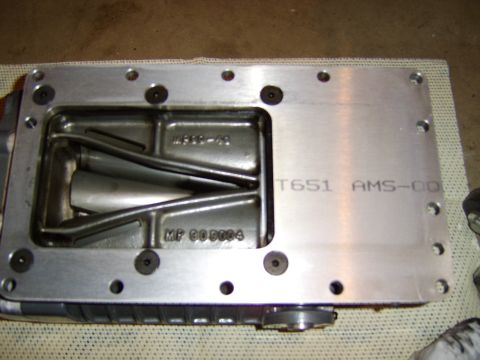1996 Mercury Grand Marquis - A machined aluminum casting, likely a supercharger or intercooler manifold cover, resting on a fabric surface. It bears cast text including…