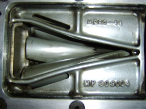 1996 Mercury Grand Marquis - Close-up of a cast aluminum part, likely an intake manifold or supercharger casting, showing internal runners and raised cast markings read…