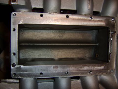 1996 Mercury Grand Marquis - Close-up of a cast aluminum intake manifold plenum with a machined rectangular opening and bolt holes around the flange, likely part of a s…