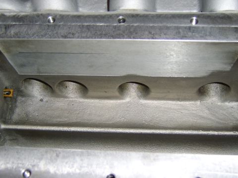1996 Mercury Grand Marquis - Close-up of a bare aluminum cast part, likely an intake manifold or valley area, showing a machined flat surface with drilled bolt holes an…