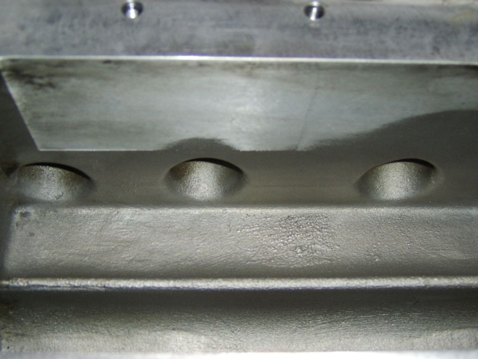 Close-up of bare aluminum casting with three round ports and machined surfaces