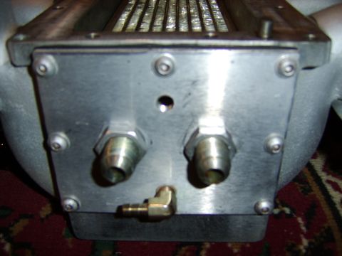 1996 Mercury Grand Marquis - Close-up of the end tank of a metal intercooler or heat exchanger, showing an aluminum end plate secured with multiple bolts, two threaded…