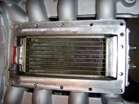 1996 Mercury Grand Marquis - Close-up of an air-to-water intercooler heat exchanger core mounted inside a cast aluminum supercharger intake manifold, showing the finned…