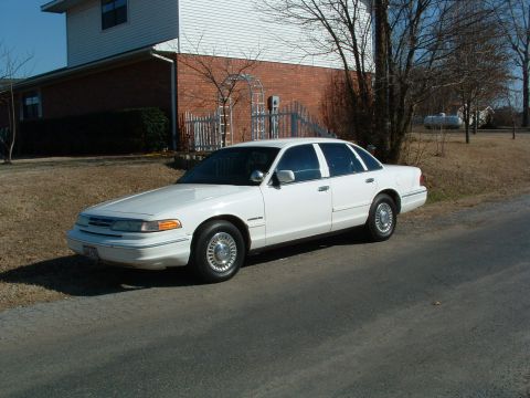1995 Ford Crown Victoria - White 1995 Ford Crown Victoria sedan parked on a paved surface in front of a house.