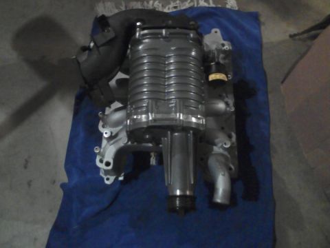 1996 Mercury Grand Marquis - An automotive supercharger unit mounted atop an aluminum intake manifold, resting on a blue moving blanket on a concrete floor. The assembl…