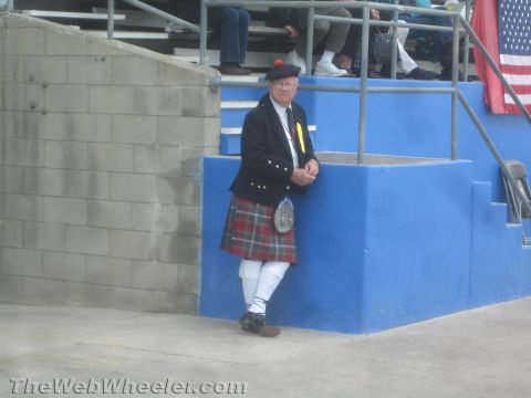 1968 Ford Mustang - Photograph of a man in a kilt and Highland jacket standing by a blue grandstand wall.