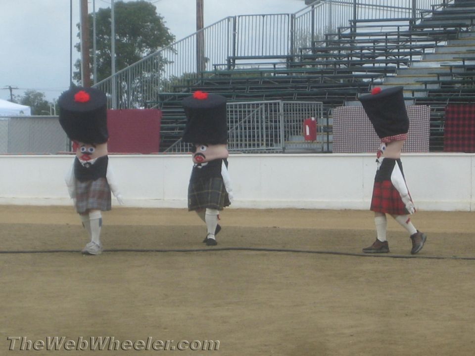 People in kilts standing in an outdoor area with a fence