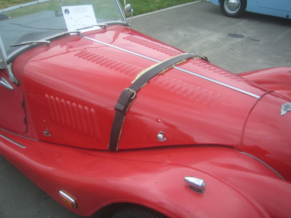 Close-up of a red Morgan roadster hood with leather bonnet strap and louvers