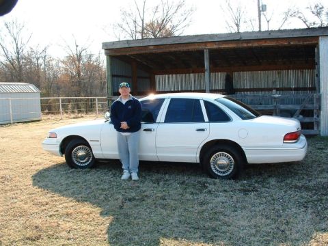 1995 Ford Crown Victoria - A man stands next to a white 1995 Ford Crown Victoria parked outdoors.
