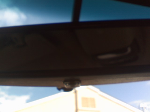Interior rearview mirror of a 1996 Ford Bronco reflecting the sky and a building.