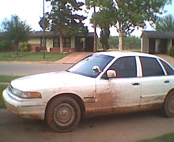 1995 Ford Crown Victoria - A white sedan is heavily covered in mud on its lower body panels and doors.