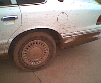 1995 Ford Crown Victoria - Mud splatters the side of a white sedan, obscuring its details.
