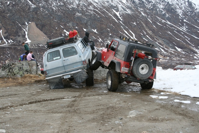 Lifted gray pickup and red Jeep navigating a rocky snowy slope