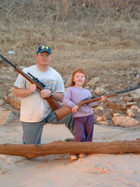 1995 Ford Crown Victoria - A man and a child pose with rifles on a beach, with a log in the foreground.