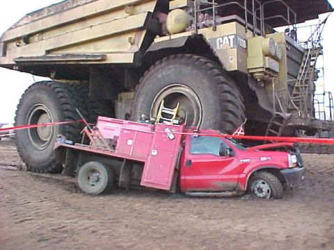 1995 Ford Crown Victoria - A red pickup truck is positioned next to a colossal yellow mining truck, highlighting the immense scale difference.