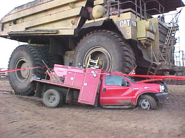 Red pickup truck dwarfed by a massive yellow CAT mining truck