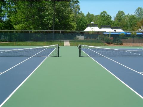 1979 Ford Ranchero - A tennis court is shown with two nets dividing the blue and green playing surfaces. In the background, trees and a building with white roof…