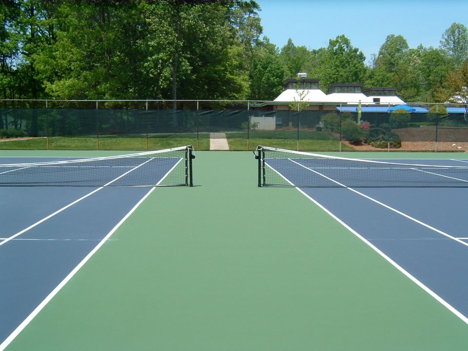 Tennis court with nets, trees, and a building.