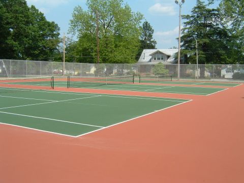 1979 Ford Ranchero - An outdoor tennis court with multiple courts visible, surrounded by a chain-link fence and trees. The courts are a mix of green playing sur…