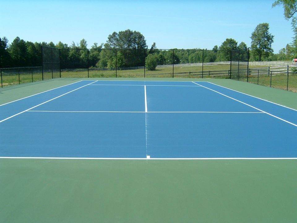 Tennis court with blue playing surface and green outer edges.