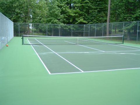 1979 Ford Ranchero - A tennis court with a net and markings is shown, surrounded by a fence and trees. A single orange tennis ball rests on the green court surf…