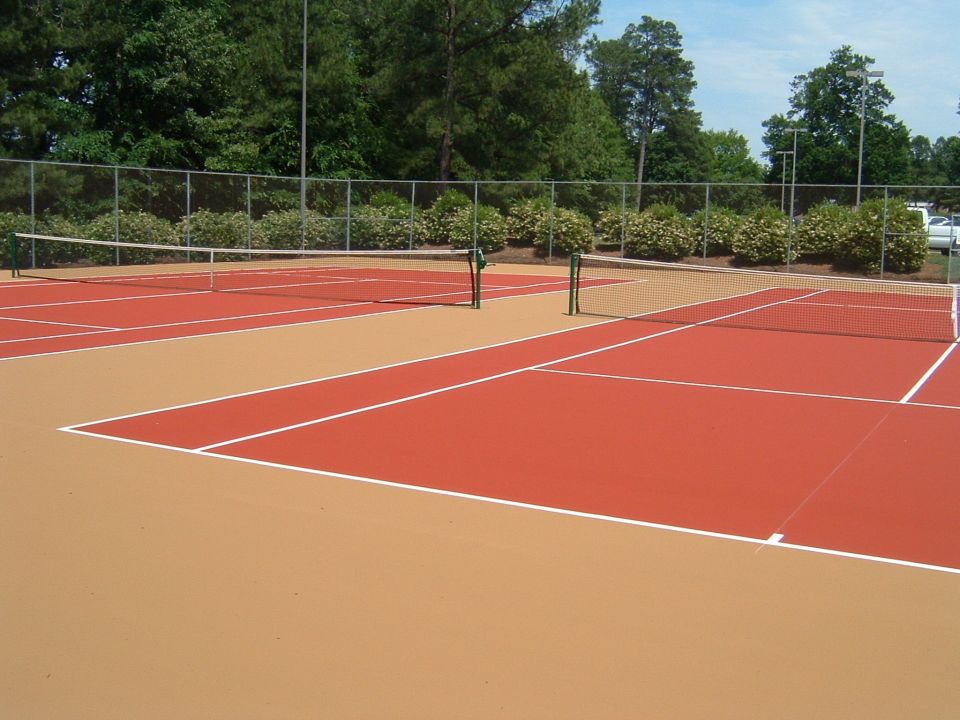Outdoor tennis court with red and tan surfaces divided by nets.