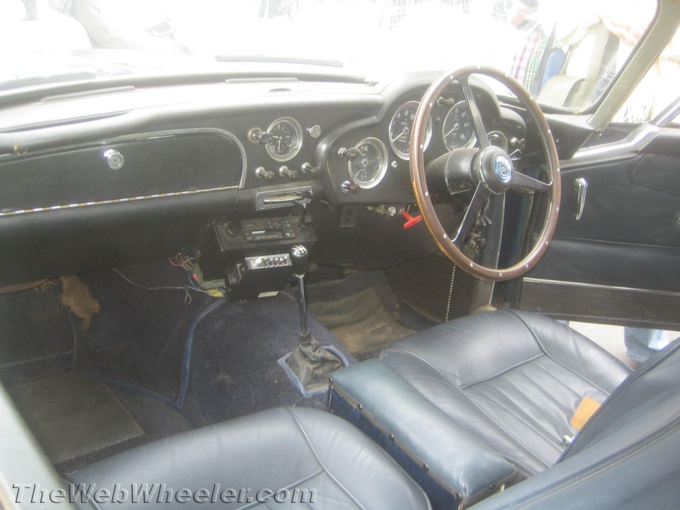 Interior of a classic Aston Martin showing wood steering wheel and dark leather seats
