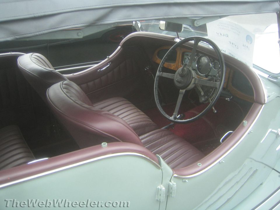 Interior of a vintage roadster with maroon leather seats and a wood-rim steering wheel