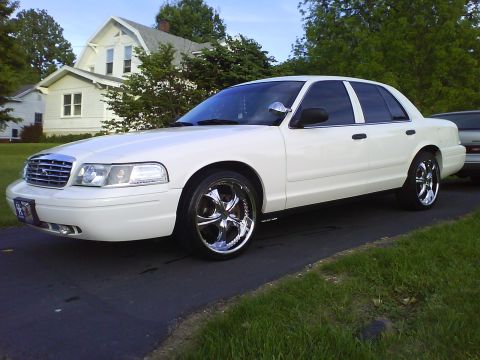 2003 Ford Crown Victoria - A white 2003 Ford Crown Victoria is parked on a driveway in front of a house. The car features chrome wheels and tinted windows.