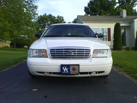 2003 Ford Crown Victoria - The front view of a white Ford Crown Victoria is shown parked on a driveway in front of a house. The vehicle has a chrome grille and a Kent…