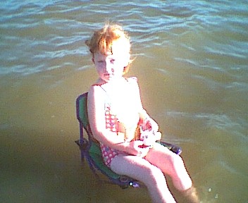1995 Ford Crown Victoria - A young child sits in a portable chair in the water, holding a stuffed animal.