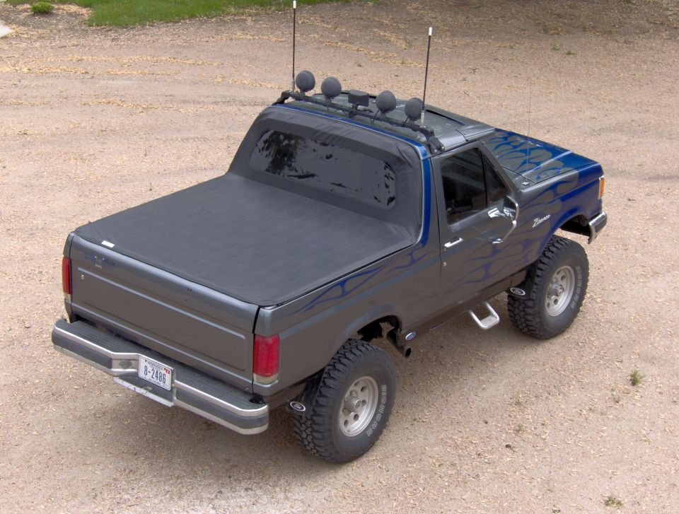 Gray Ford Bronco with blue flames, tonneau cover and roof light bar, rear view