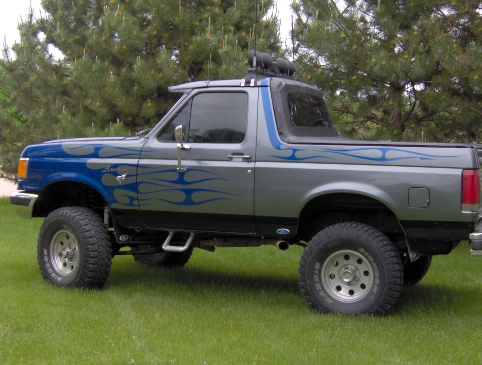 Lifted Ford Bronco with gray and blue flame paint parked on grass