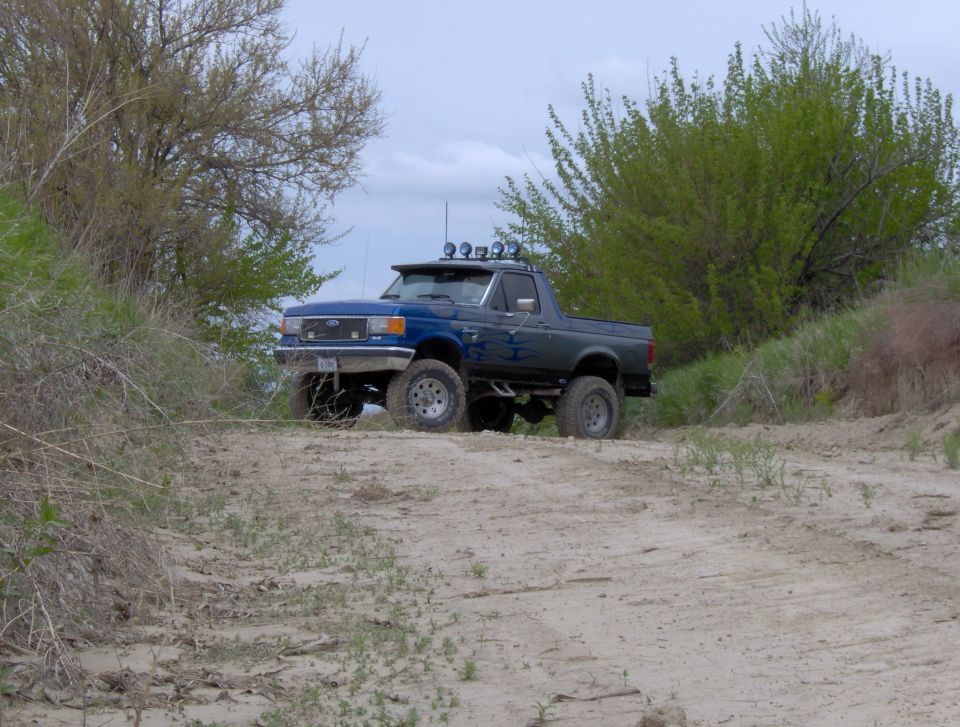 Lifted dark blue 1987 Ford Bronco with flame decals on a sandy trail.