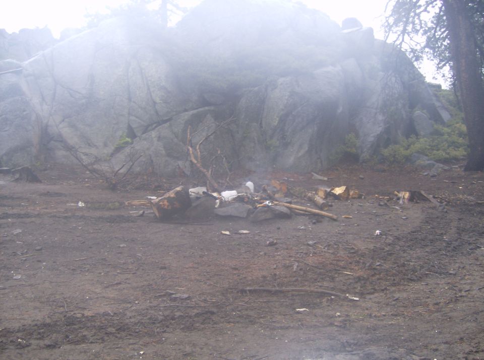 Campfire pit filled with trash and debris in front of a rock formation.