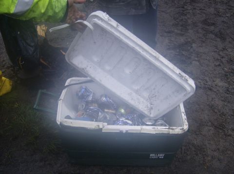 1986 Ford Bronco - A person in a green jacket is holding the lid of a cooler filled with crushed aluminum cans. The cooler is dark green with the brand name "…