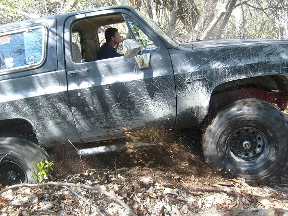 Side view of a dark 1979 Chevrolet Blazer driving off-road, kicking up mud.