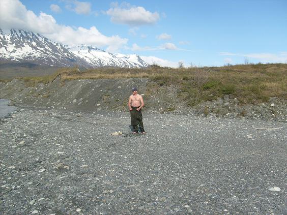 A man on a rocky shore with mountains.
