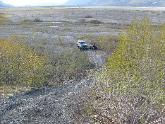 Dark SUV and red ATV parked on a gravel road in a natural landscape.