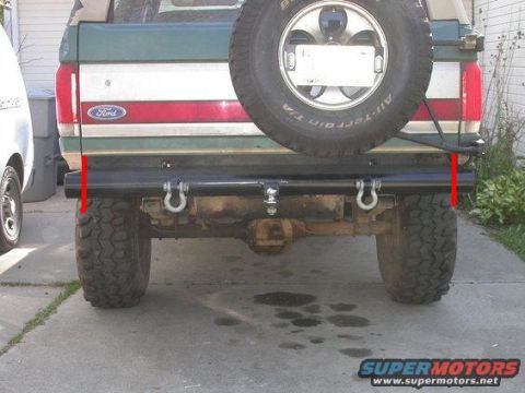 1990 Ford Bronco - The rear view of a green and white Ford Bronco is shown, featuring a spare tire mounted on the back and a black aftermarket bumper with tow…